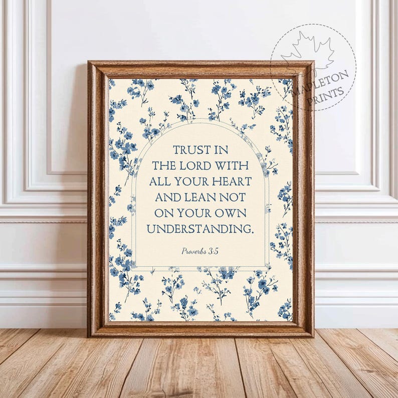 May include: Framed print featuring the text "TRUST IN THE LORD WITH ALL YOUR HEART AND LEAN NOT ON YOUR OWN UNDERSTANDING." The artwork has a cream background with blue floral accents and a wooden frame. The text is in a serif font.