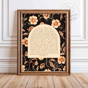 May include: A framed print with a black background and gold floral accents. The print features a passage from the Bible, Matthew 5:3-12, about the Beatitudes. The text is in a white font and is surrounded by a decorative arch.
