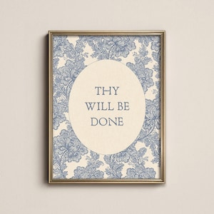 May include: A rectangular wall art print in a gold frame featuring a cream-colored oval center with the text THY WILL BE DONE in blue. The background surrounding the oval consists of a detailed blue floral lace pattern on a cream base.