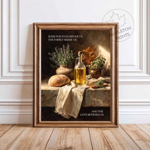 Könnte beinhalten: Ein gerahmter Kunstdruck mit einem Stillleben mit Brot, Öl und Kräutern. Das Kunstwerk hat eine warme Farbpalette und enthält den Text "BLESS THE FOOD BEFORE US, THE FAMILY BESIDE US, AND THE LOVE BETWEEN US."