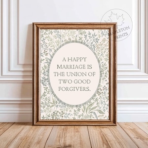 May include: Framed print with the text "A HAPPY MARRIAGE IS THE UNION OF TWO GOOD FORGIVERS." The print has a light beige background with a floral design in shades of green and gray. The frame is a warm brown color.