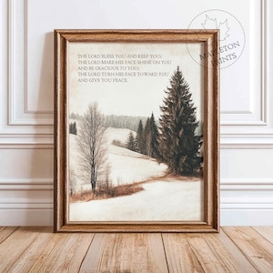 May include: A framed print with a wintery landscape scene of snow-covered hills and pine trees. The print features a quote: "The Lord bless you and keep you: The Lord make his face shine on you and be gracious to you: The Lord turn his face toward you and give you peace."