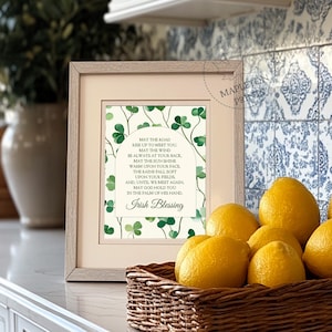 May include: A framed print with a white background and green shamrocks. The print features an Irish blessing that reads: "May the road rise up to meet you. May the wind be always at your back. May the sun shine warm upon your face. The rains fall soft upon your fields. And, until we meet again, may God hold you in the palm of his hand. Irish Blessing."