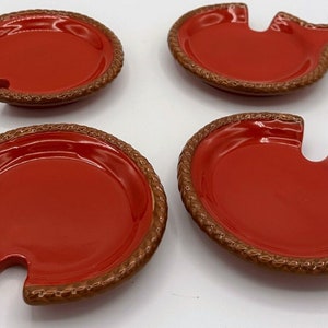 May include: Set of four red ceramic serving dishes with a brown rope design around the edge. Each dish has a small cutout on the side.