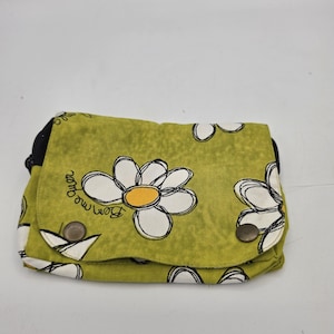 May include: A rectangular fabric pouch in olive green featuring a repeating pattern of white daisies with yellow centers and black outlines. The flap includes two dark metal snap buttons and the text "bem me quer" printed in black script.