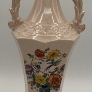 May include: A pink ceramic vase with gold accents and floral designs. The vase has two handles and a wide base.