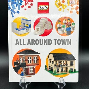 May include: A white hardcover book titled LEGO ALL AROUND TOWN featuring a red LEGO logo at the top. The cover displays five circular images of various LEGO brick structures, including a kitchen, a bridge, a store counter, and two houses.