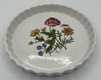 May include: A round white ceramic fluted tart dish featuring a central botanical illustration. The design includes a large purple poppy, a yellow sunflower, small blue flowers, green foliage, and two small butterflies with delicate wings.