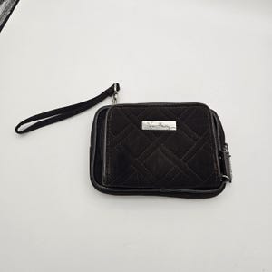 May include: A black quilted wristlet wallet featuring a rectangular shape, a detachable wrist strap, and a silver-toned metal plaque on the front with the text Vera Bradley engraved. The wallet has a zippered closure and a diamond-stitched pattern.