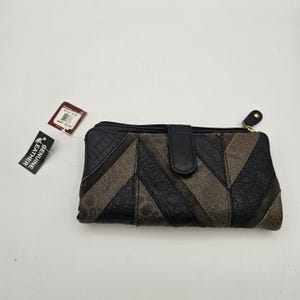 May include: A rectangular genuine leather wallet featuring a diagonal patchwork design in alternating shades of black and dark gray. The wallet includes a central snap-button closure, a top zipper with a black pull tab, and two attached product tags.