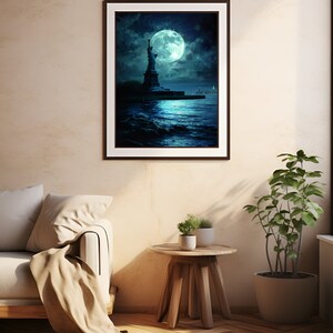 Op de afbeelding: Een ingelijste kunstdruk met het Vrijheidsbeeld onder een grote, stralende maan. Het kunstwerk gebruikt blauwe en zeegroene tinten, met het beeld als silhouet tegen de nachthemel. De print hangt aan een beige muur, naast een bank en een kleine houten tafel.