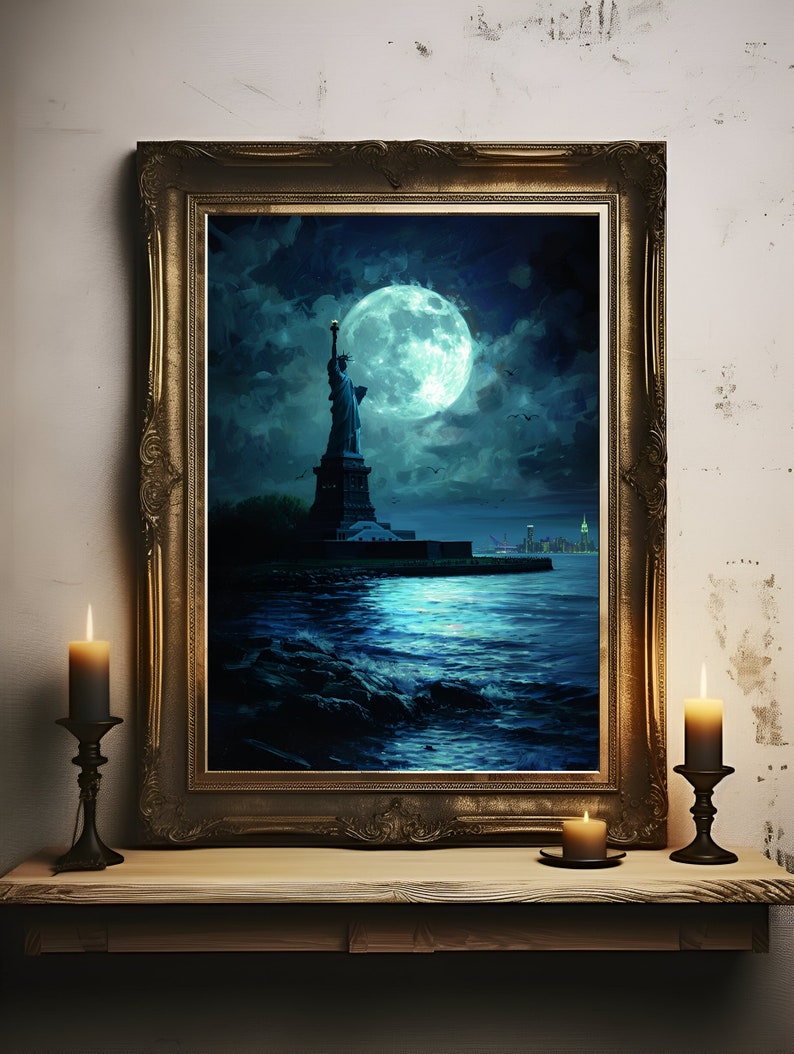 Op de afbeelding: Een ingelijst kunstwerk met het Vrijheidsbeeld onder een grote, gloeiende maan. Het schilderij heeft een donker, sfeervol kleurenpalet met tinten blauw en teal. De lijst is goudkleurig. Twee brandende kaarsen in zwarte houders staan op een houten plank.