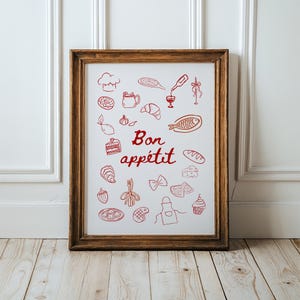 May include: A framed print with a white background and red illustrations of various food items, including a fish, a loaf of bread, a glass of wine, and a pastry. The text "Bon appétit" is written in red cursive lettering.