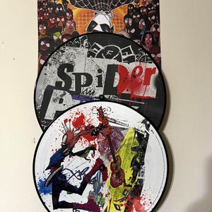 May include: Two black and white vinyl records with a Spider-Man theme. The top record has the word "Spider" in large, bold letters. The bottom record features a cartoon character playing a guitar with red, yellow, and blue paint splatters.