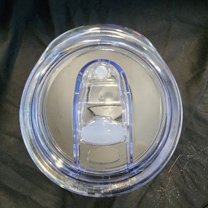 Op de afbeelding: Transparante plastic tumblerdeksel met een schuifsluiting. Het deksel heeft een helder, afgerond ontwerp met een lichtblauwe accentrand en een transparant schuifmechanisme. Het deksel is ontworpen om op een tumbler te passen.