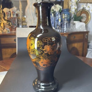 Peut inclure: Un vase en céramique noire avec un motif de dragon doré. Le vase a un col étroit et une base large.