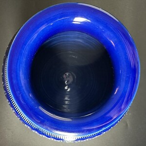 May include: A top-down view of a deep blue ceramic vase. The vase has a wide, rounded rim and a textured interior. The rim is a brighter shade of blue than the interior. The vase has a decorative pattern around the outside.