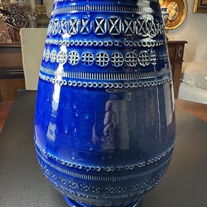 May include: A large, cobalt blue ceramic vase with a glossy finish. The vase features intricate, geometric patterns and perforations around the body. The design includes rows of circles, crosses, and other shapes. The vase has a wide base and a slightly flared top.