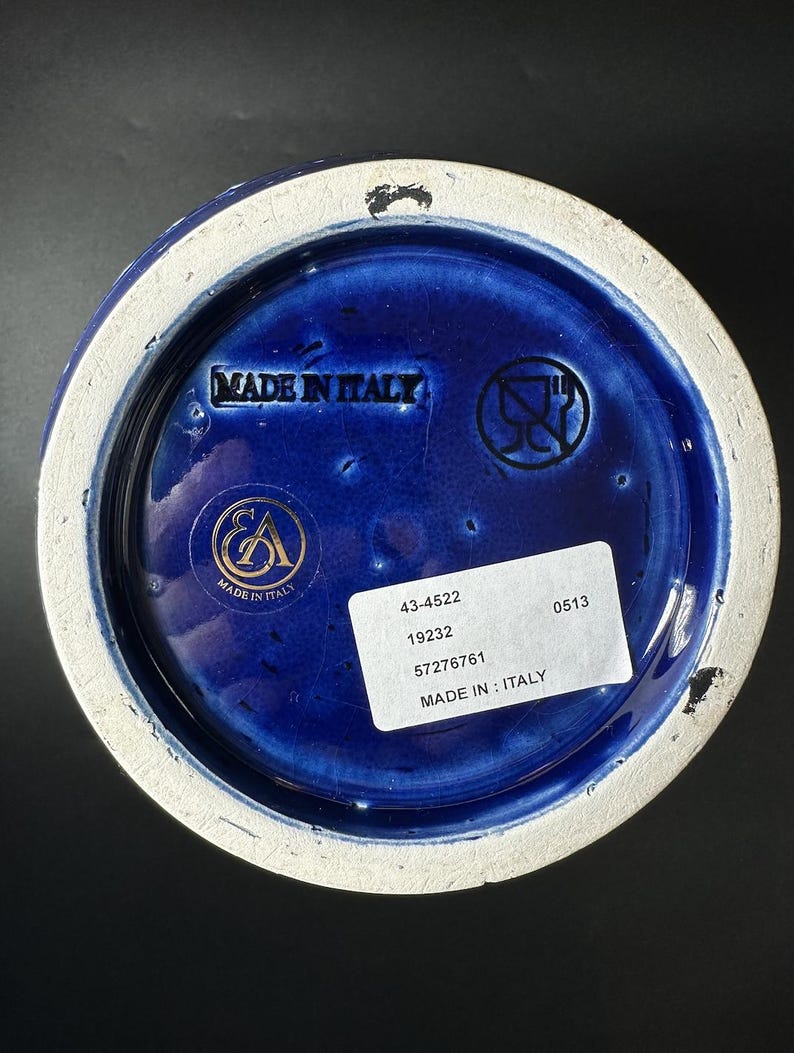 May include: Close-up of the base of a ceramic vase. The interior is a deep blue with a white rim. The base has the text "MADE IN ITALY" and a sticker with numbers. The vase has a glossy finish.