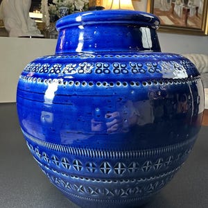 May include: A large, cobalt blue ceramic vase with a lid. The vase features a glossy finish and is adorned with intricate patterns of small holes and cross-like designs. The vase has a bulbous body and a cylindrical neck.