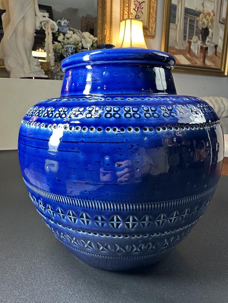 May include: A large, cobalt blue ceramic vase with a lid. The vase features a glossy finish and is adorned with intricate patterns of small holes and cross-like designs. The vase has a bulbous body and a cylindrical neck.