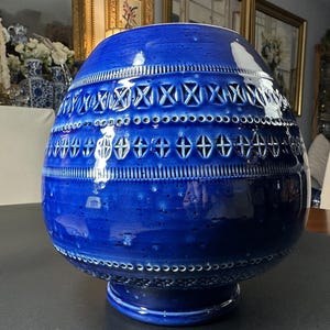 May include: A large, cobalt blue ceramic vase with a bulbous shape and a pedestal base. The vase features intricate cut-out designs and textured bands around the body. The vase is approximately 14 inches tall.