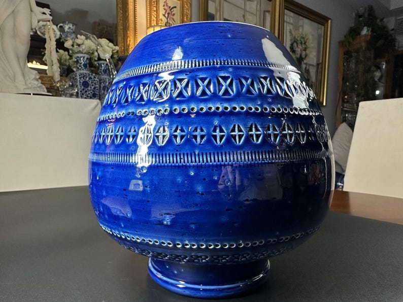 May include: A large, cobalt blue ceramic vase with a bulbous shape and a pedestal base. The vase features intricate cut-out designs and textured bands around the body. The vase is approximately 14 inches tall.