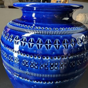 May include: A large, cobalt blue ceramic vase with a glossy finish. The vase features intricate geometric patterns, including rows of small circles, vertical lines, and diamond-shaped designs. The vase has a wide base and a flared rim, making it a decorative home accent.