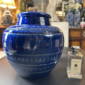 May include: A large, glossy, cobalt blue ceramic vase with a decorative pattern of small circles and geometric shapes. A Jo Malone cologne bottle is next to the vase.