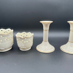 May include: Set of four ivory porcelain candle holders with gold trim. Two are tall candle holders with a floral design and two are shorter, open-work candle holders.