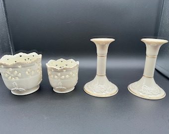 May include: Set of four ivory porcelain candle holders with gold trim. Two are tall candle holders with a floral design and two are shorter, open-work candle holders.