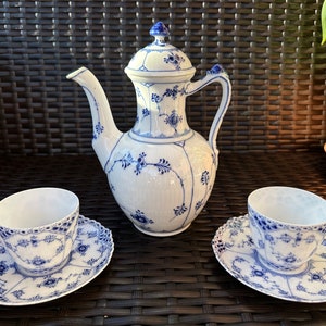 Könnte beinhalten: Ein blaues und weißes Porzellan-Tee-Set mit einer Teekanne, zwei Tassen und zwei Untertassen. Das Set hat ein zartes Blumenmuster und einen blauen und weißen Rand.