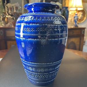May include: A cobalt blue ceramic vase with a wide body and a narrow neck. The vase features intricate embossed geometric patterns and a glossy finish. The vase is a decorative item, suitable for displaying flowers or as a standalone art piece.