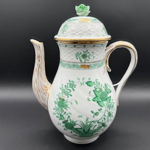May include: A white porcelain coffee pot with a green and gold floral design. The pot has a lid with a small green rose on top.