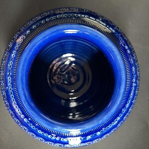 May include: A top-down view of a deep blue ceramic bowl. The bowl has a wide, textured rim with a repeating pattern of small, white dots. The interior is a darker shade of blue, with a glossy finish. The bowl's design is simple and elegant.