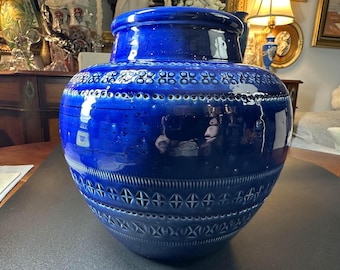 May include: A large, cobalt blue ceramic vase with a glossy finish. The vase features intricate geometric patterns around the neck and body, including rows of small circles and cross-like shapes. The vase has a wide, rounded body and a slightly flared rim.