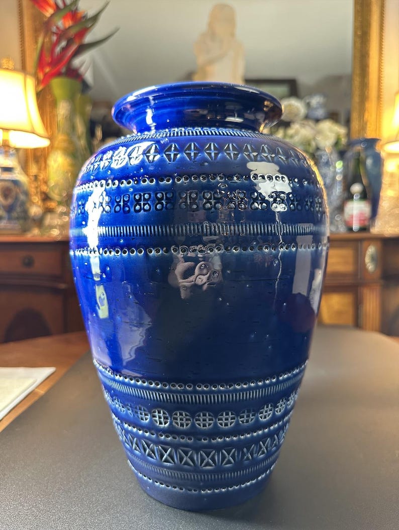 May include: A cobalt blue ceramic vase with a textured surface and decorative patterns. The vase features a wide body and a slightly flared rim. The patterns include geometric shapes and lines. The vase is a decorative home decor item.