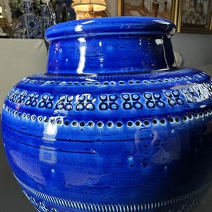 May include: A large, cobalt blue ceramic vase with a wide, rounded body and a slightly narrower neck. The vase features a series of decorative patterns, including rows of small circles and stylized geometric shapes. The glossy finish enhances the rich color.