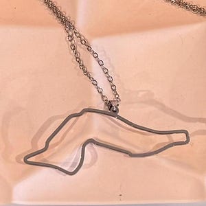 May include: A silver necklace with a pendant shaped like the outline of a country. The pendant is made of metal and has a shiny finish.