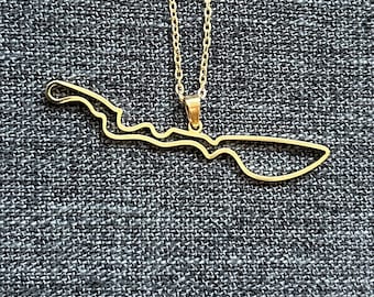 May include: A gold necklace with a pendant shaped like the outline of an island. The necklace is on a gray fabric background.
