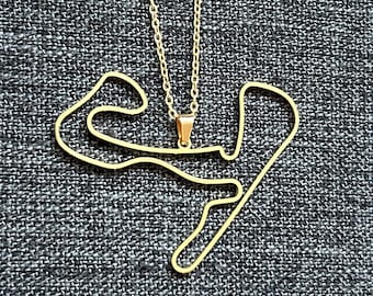Puede incluir: Un collar de oro con un colgante con forma de circuito de carreras.