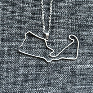 Peut inclure: Un collier en argent avec un pendentif en forme de circuit de course.