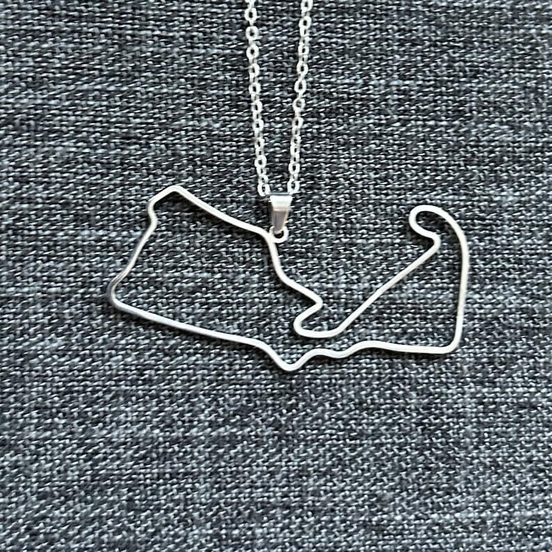 Peut inclure: Un collier en argent avec un pendentif en forme de circuit de course.