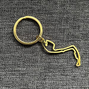 Può includere: Un portachiavi dorato con un contorno dettagliato di uno stato o una regione. Il portachiavi ha un anello semplice per attaccarlo alle chiavi.