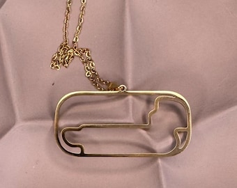 Könnte beinhalten: Eine goldene Halskette mit einem Anhänger in Form einer Rennstrecke. Der Anhänger ist eine einfache Umrandung einer Rennstrecke.