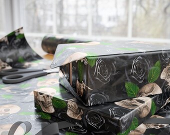 Könnte beinhalten: Zwei verpackte Geschenke mit schwarzem Geschenkpapier mit einem Totenkopf- und Rosenmuster. Grüne Blätter und graue Rosen akzentuieren das Design. Eine Schere und eine Rolle Geschenkpapier sind im Hintergrund zu sehen.