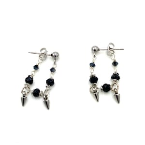 May include: A pair of silver-tone earrings with a dangling design. Each earring features a post with a small ball, a chain of small black beads, larger black beads, and two silver-tone cone-shaped spikes. The earrings are displayed against a white background.