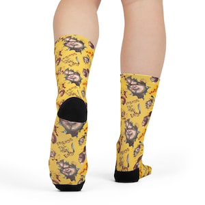 May include: Yellow crew socks featuring a repeating pattern of a doll face, blood splatters, a knife, and the text "FRIENDS TILL THE END" in black lettering. The socks have solid black heels and toes, providing a contrast to the bright yellow fabric.