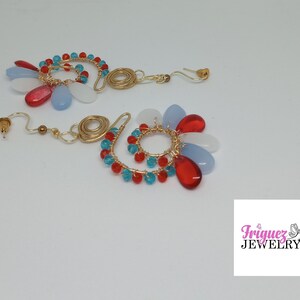May include: A pair of gold-toned wire earrings with a spiral design. Each earring features a cluster of red, blue, and white teardrop-shaped beads and smaller turquoise beads. The earrings have a post-back closure.