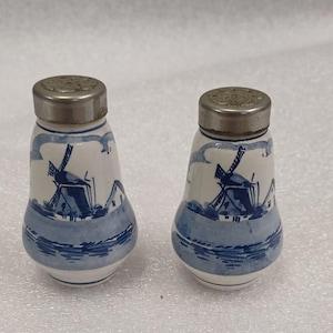 May include: A pair of blue and white ceramic salt and pepper shakers with a windmill design. The shakers have silver lids.